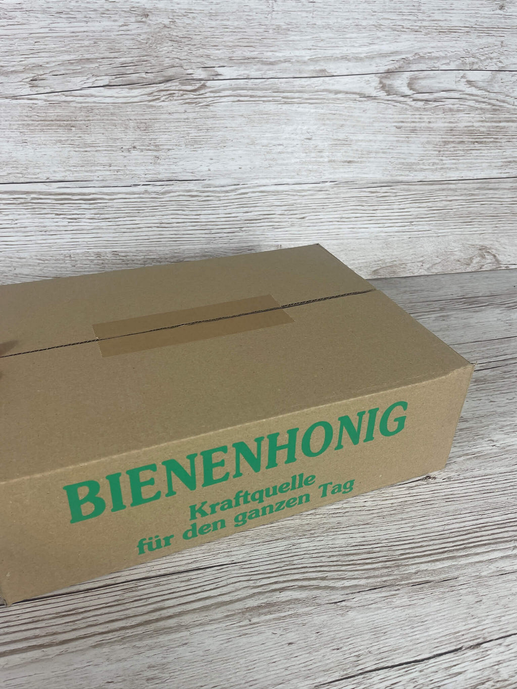 Geschlossener brauner Versandkarton für Honiggläser mit grünem Aufdruck Bienenhonig Kraftquelle für den ganzen Tag