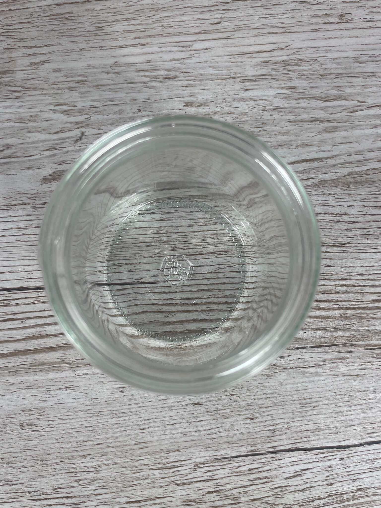 Direkte Draufsicht in ein leeres Neutralglas 500g mit Sicht auf das geprägte Glaslogo am Flaschenboden