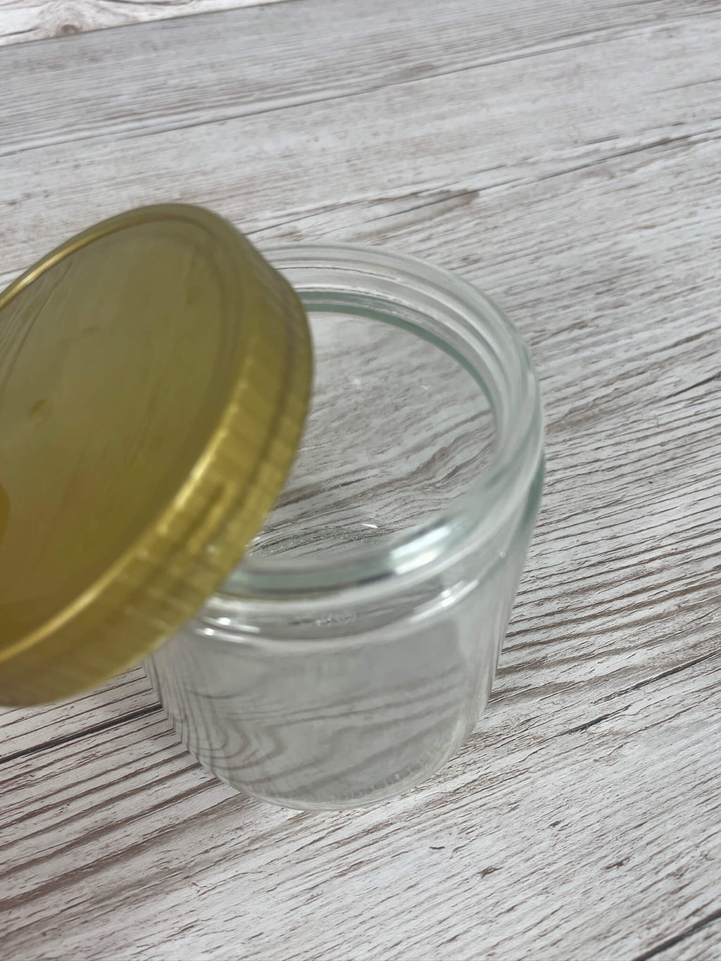 Leeres Neutralglas 500 g für Honig mit schräg aufgelegtem goldenem Schraubdeckel TO80 auf Holzhintergrund