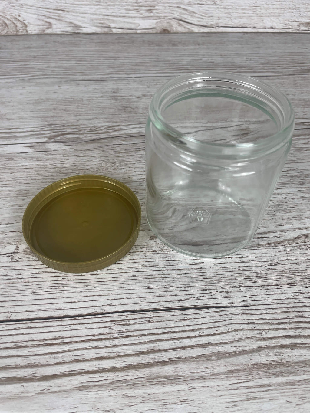 Leeres 500g Neutralglas in der Draufsicht mit separat danebenliegendem goldenem 80er Schraubdeckel