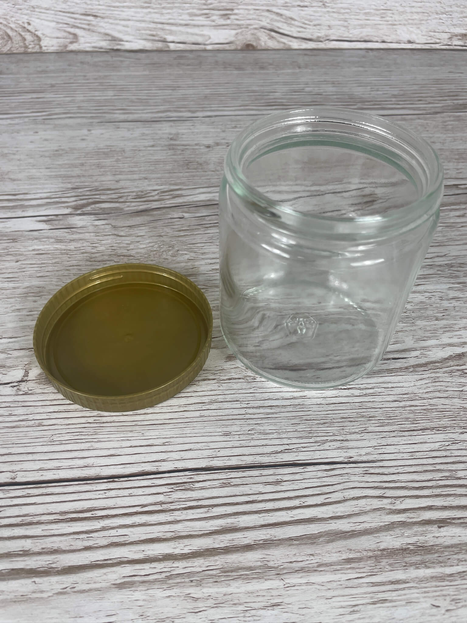 Leeres 500g Neutralglas in der Draufsicht mit separat danebenliegendem goldenem 80er Schraubdeckel