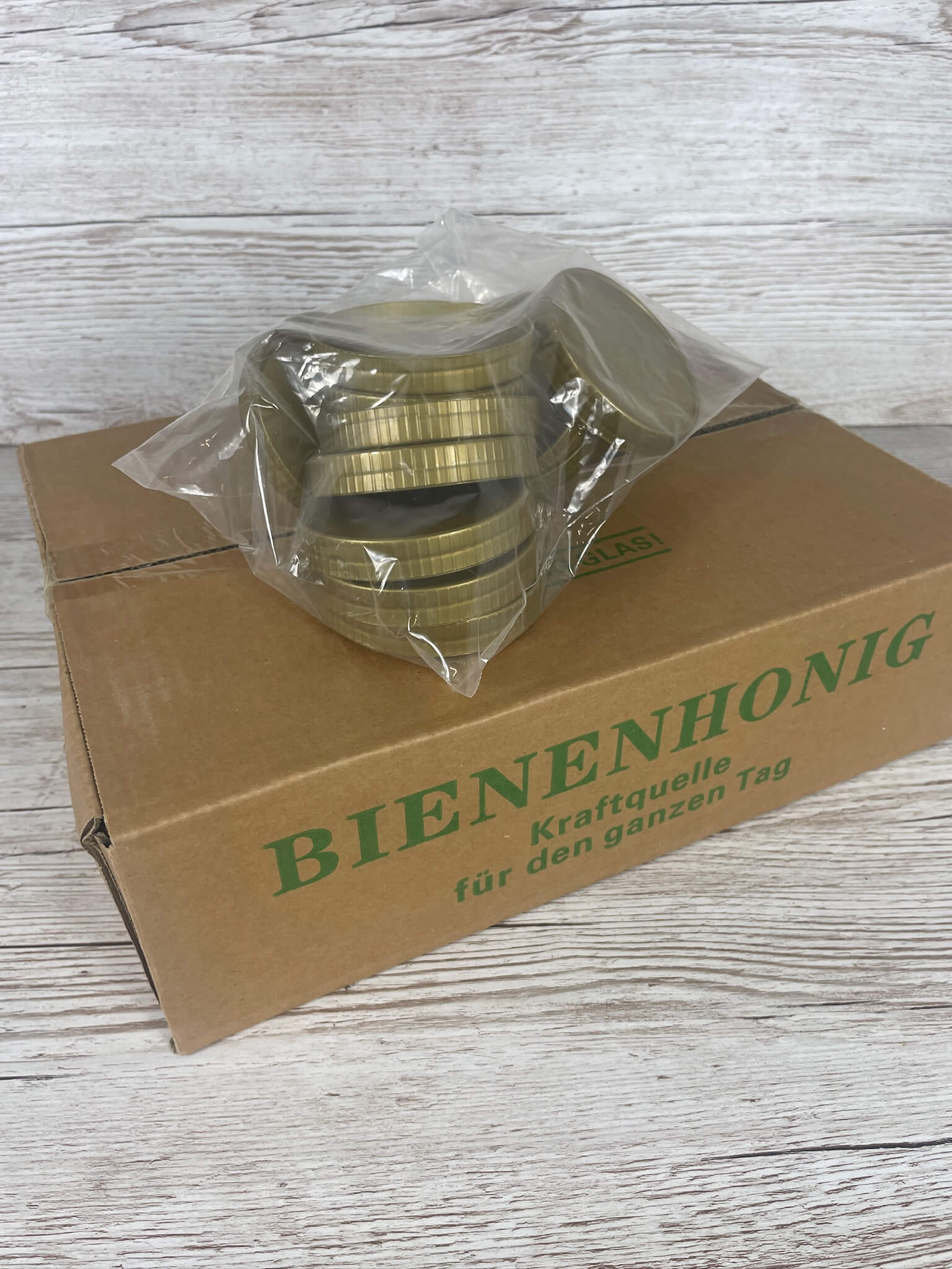 Brauner Bienenhonig-Karton für 500g Gläser mit einem aufliegenden Plastikbeutel voller goldener Schraub-Deckel